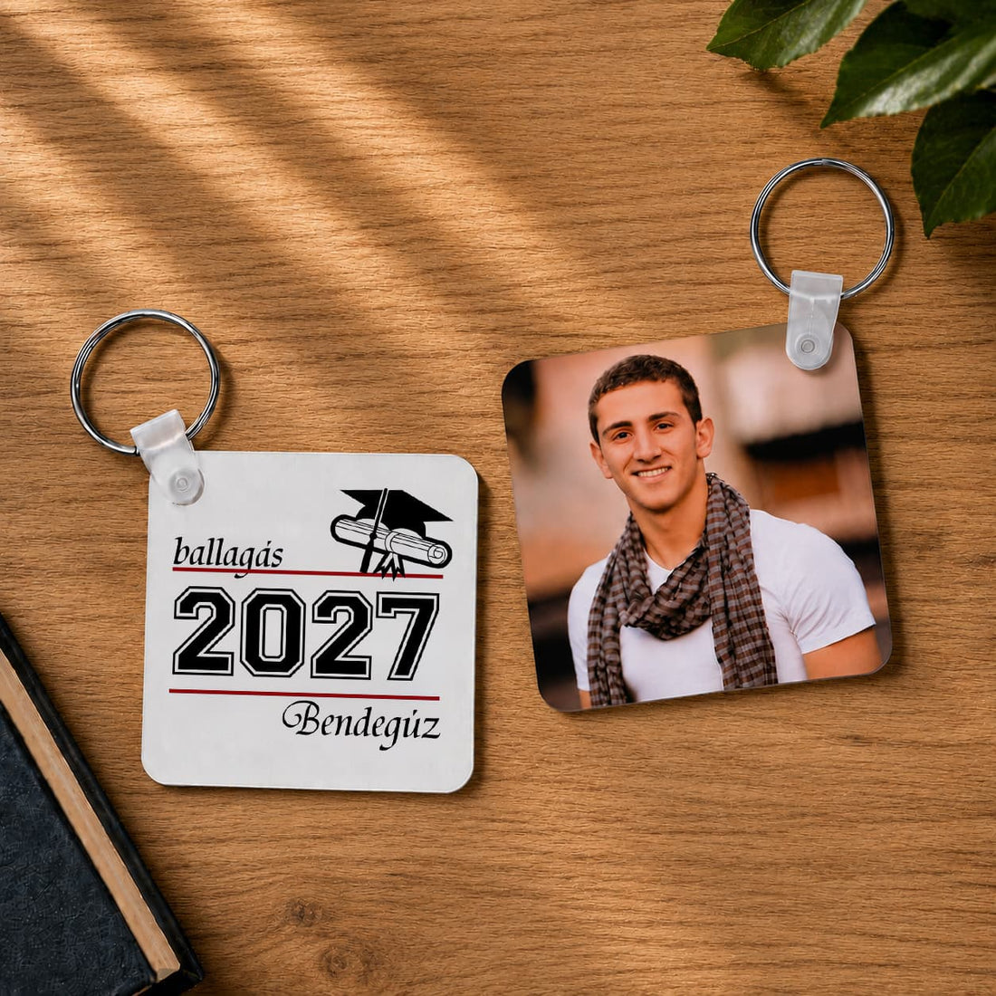 „Ballagás 2027” feliratú és fényképes négyzet alakú kulcstartók Bendegúz névvel, meleg fa háttéren.