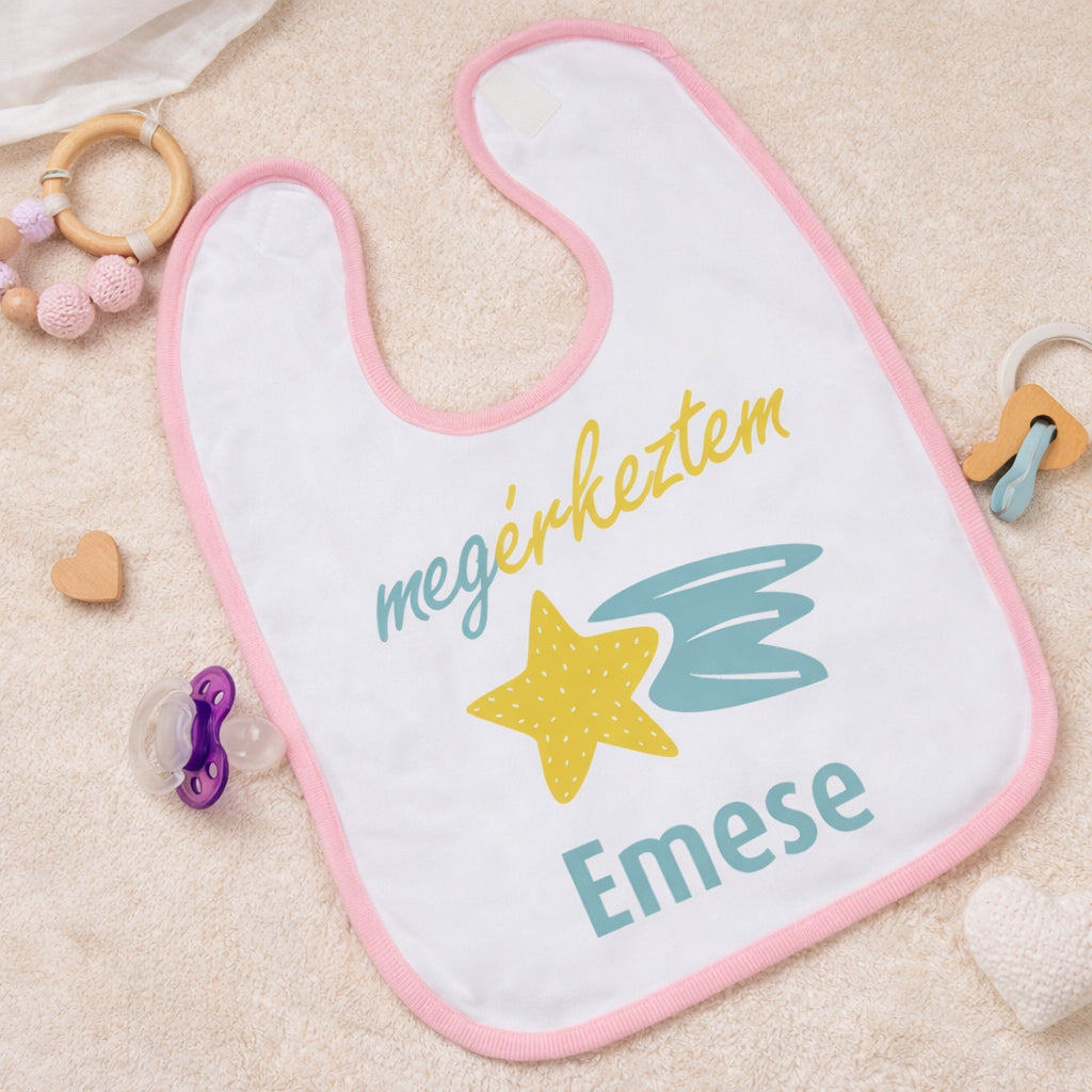 Egyedi „Megérkeztem” feliratú baba előke rózsaszín szegéllyel, sárga hullócsillag grafikával és cserélhető keresztnévvel, bézs háttéren esztétikusan elrendezve.