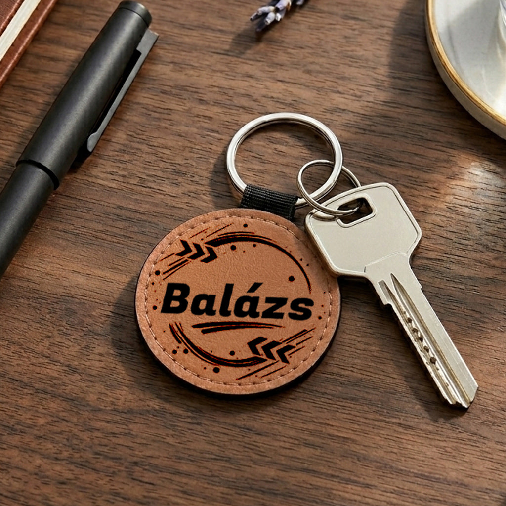 Egyedi névreszóló barna színű bőr kulcstartó saját névvel és modern grafikával, krómozott fém kulcskarikával és kulccsal, fa asztali környezetben fotózva. Praktikus és személyes ajándék férfiaknak és nőknek.