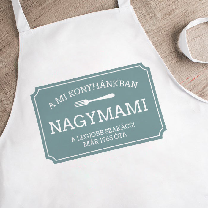 Egyedi fehér kötény „A MI KONYHÁNKBAN” fix felirattal és 3 sor személyre szabható szöveggel – vintage stílusú ajándék nagymamának, anyának vagy hobbiszakácsoknak.