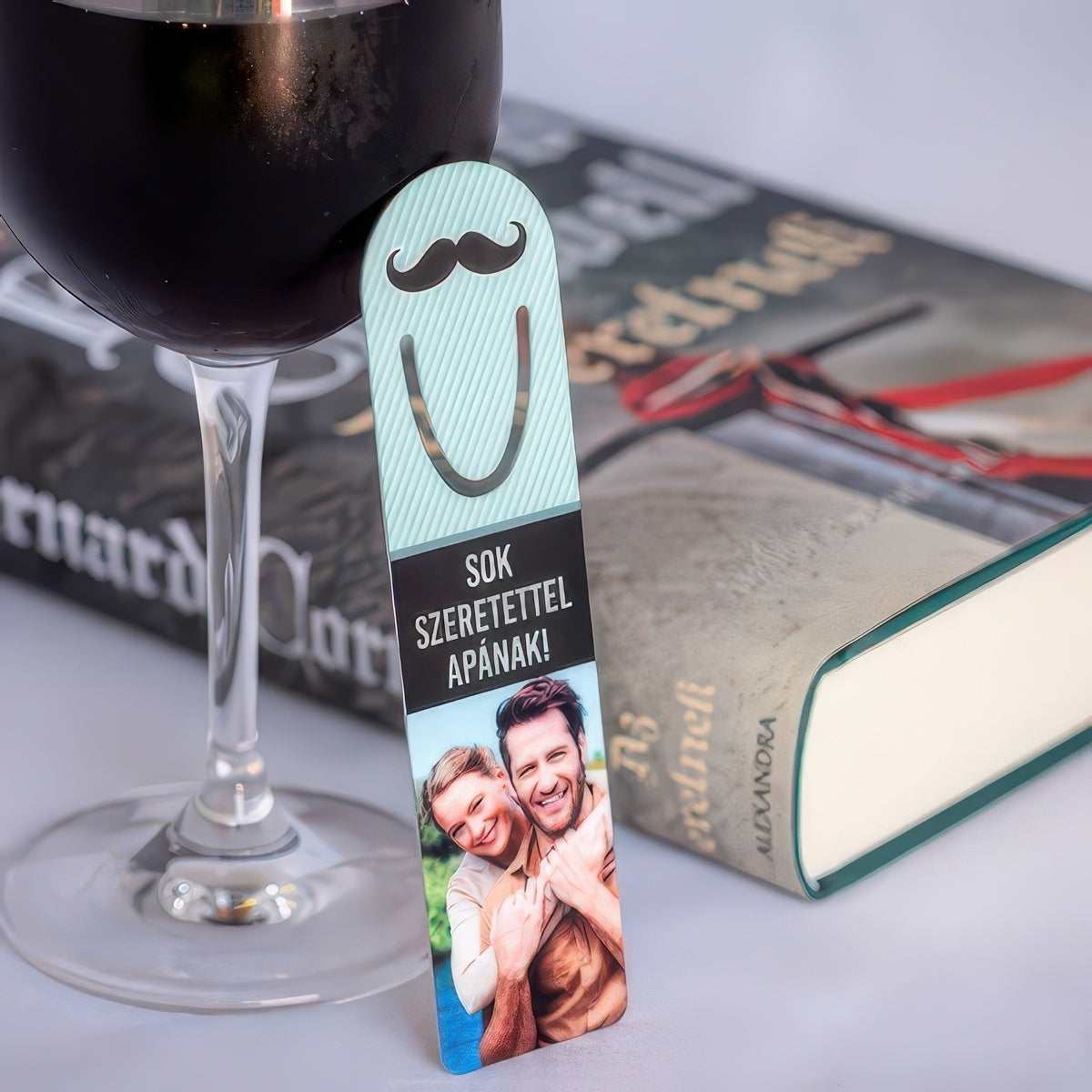 Bajusz mintás fém könyvjelző egyedi fényképpel és felirattal, ahol a kép és a szöveg szabadon cserélhető, humoros és személyes ajándék könyvrajongóknak.
