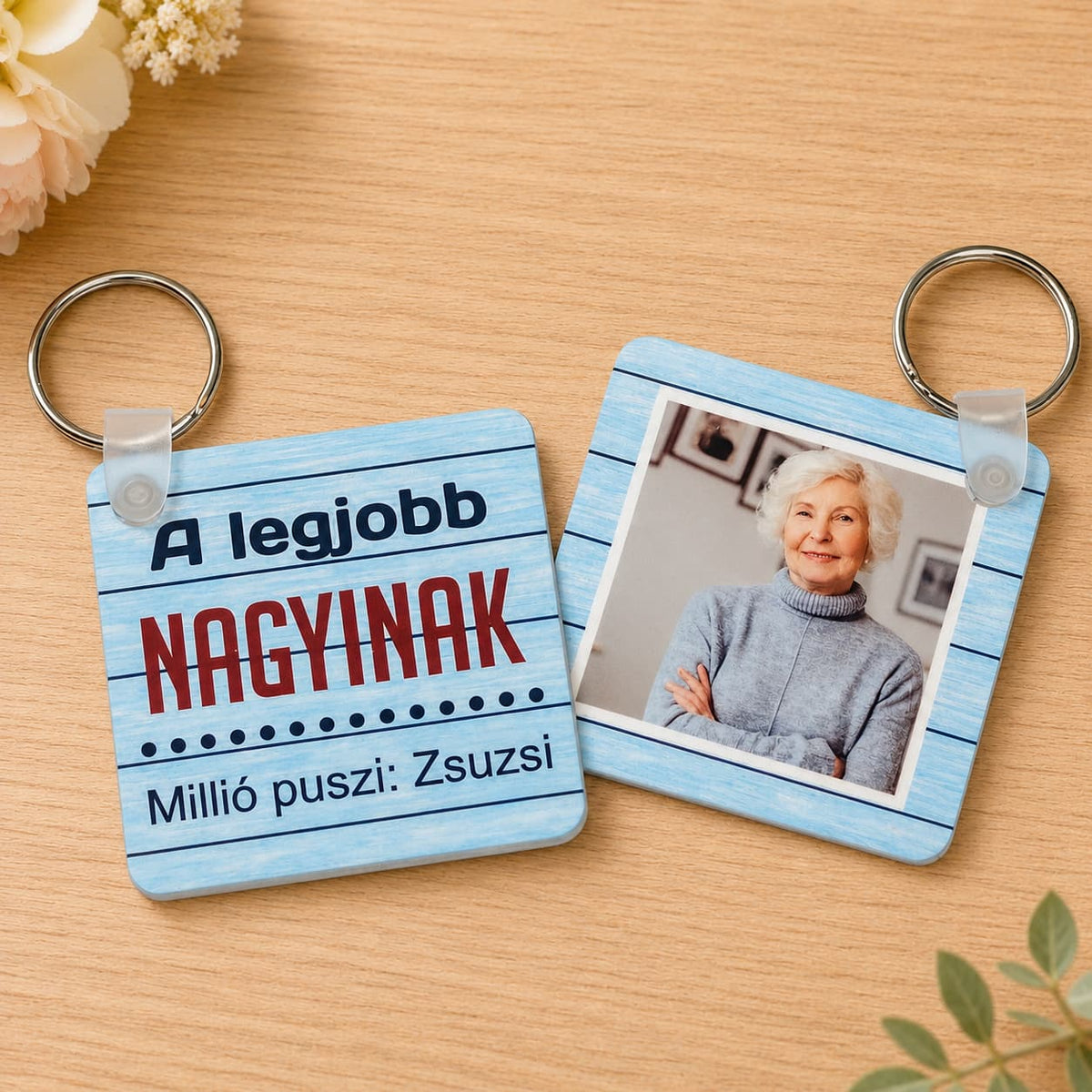 „A legjobb nagyinak” feliratú és nagymama fotójával készült egyedi fényképes kulcstartók, világos fa háttéren.