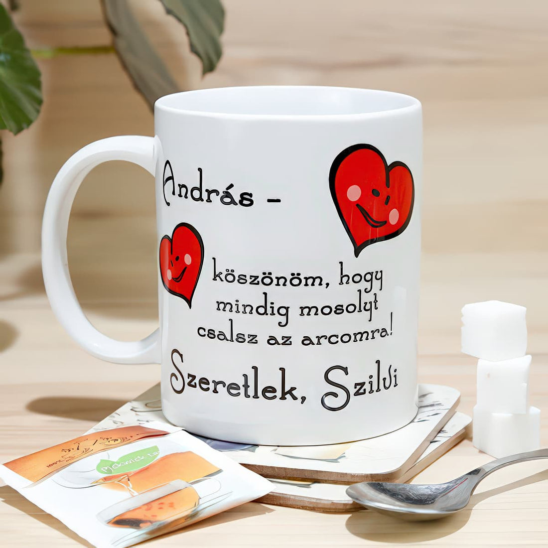 Fehér bögre két mosolygó piros szívvel, „András, köszönöm, hogy mindig mosolyt csalsz az arcomra! Szeretlek, Szilvi” felirattal