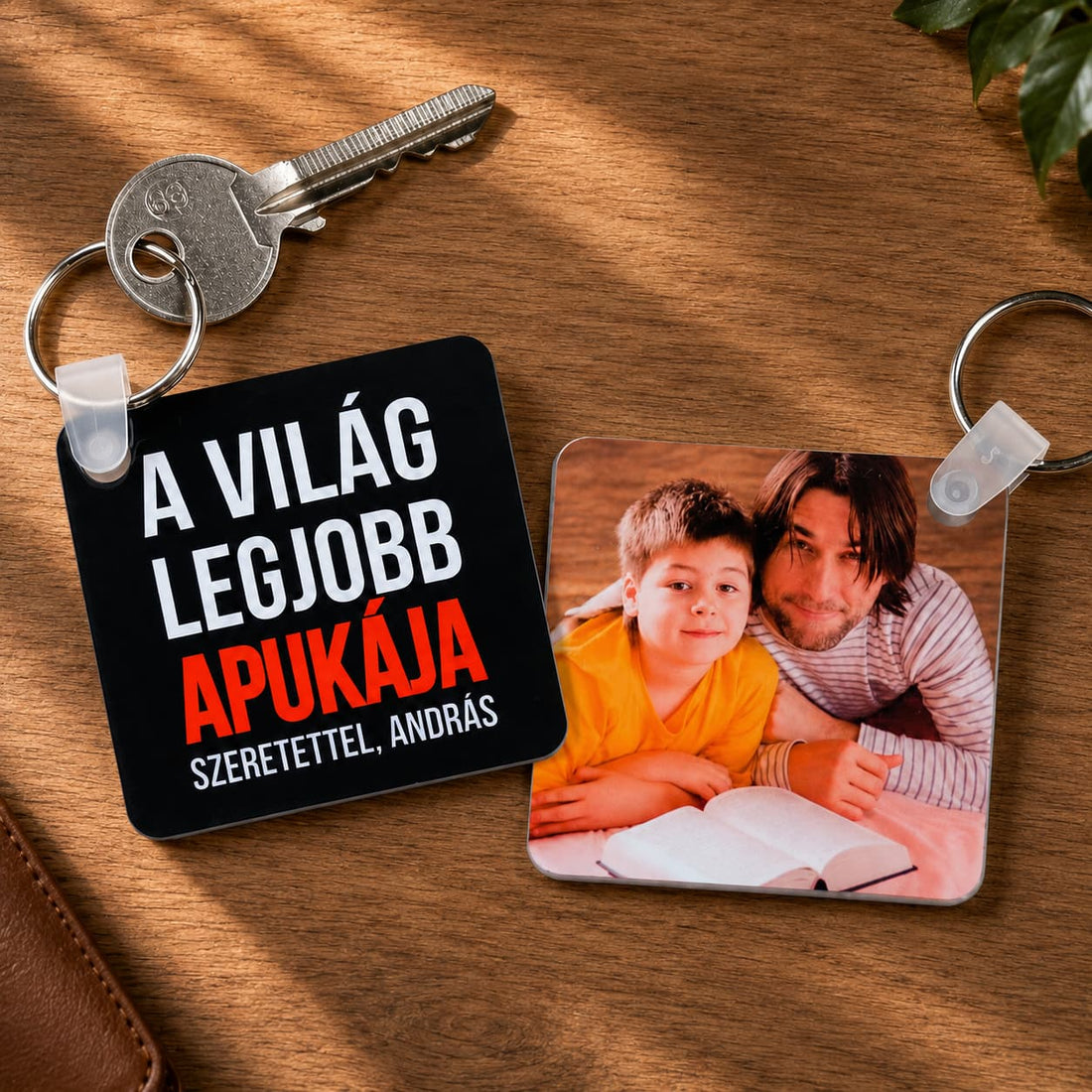 „A világ legjobb apukája” feliratú és apa–fia fotós négyzet alakú kulcstartók, meleg fa háttéren.