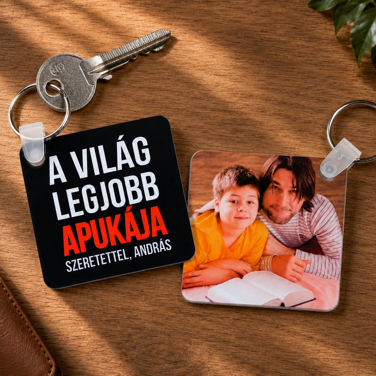 „A világ legjobb apukája” feliratú és apa–fia fotós négyzet alakú kulcstartók, meleg fa háttéren.